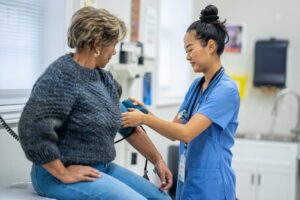 Medical assistant uses blood pressure cuff on patient in exam room