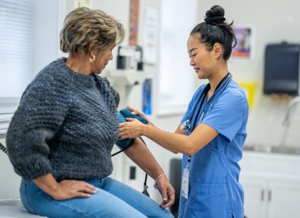 Medical assistant uses blood pressure cuff on patient in exam room