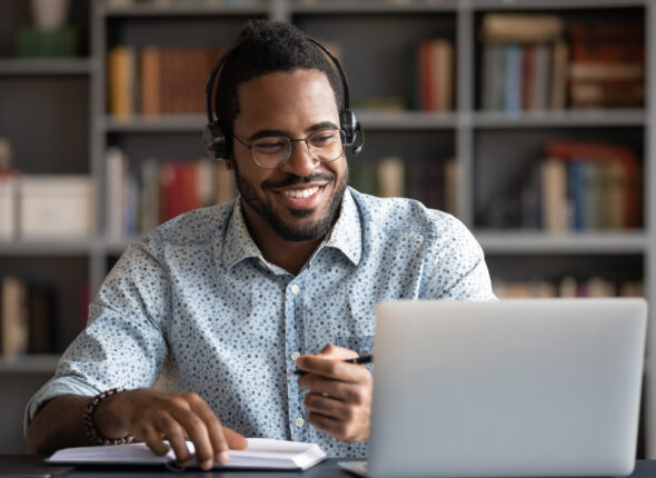 Smiling,African,American,Man,Wearing,Headphones,Looking,At,Laptop,Screen,