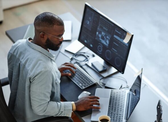 IT support specialist works with two computers at desk