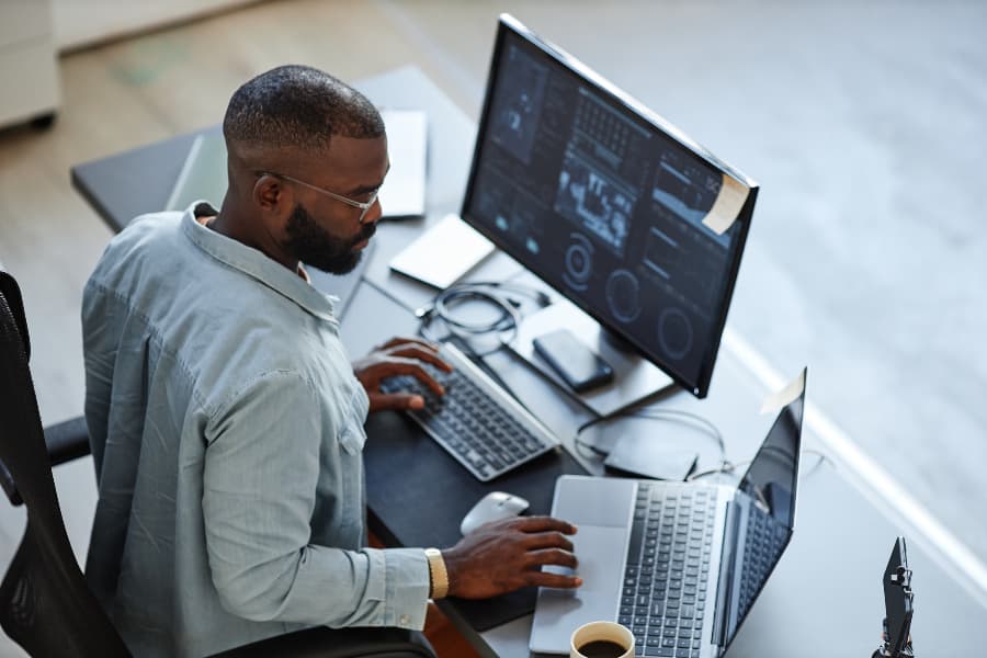 IT support specialist works with two computers at desk