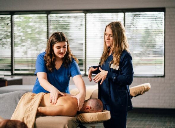 Unitech Training academy massage therapy student practicing back massage techniques with client under instructor’s supervision.