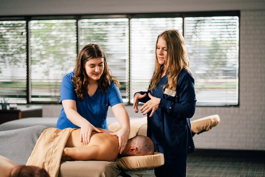 Unitech Training academy massage therapy student practicing back massage techniques with client under instructor’s supervision.